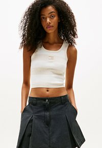 Top sin mangas a rayas blancas y beige con un diseño ajustado, combinado con una falda de mezclilla negra con pliegues y bolsillos laterales.
