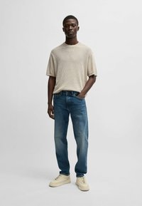 Camisa de punto de manga corta color beige con relieve, jeans azules de corte relajado y zapatillas beige. Diseño sencillo y textura suave en toda la prenda.