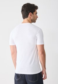 White short-sleeve t-shirt, fitted design, soft cotton texture, round neck, complementary stitching, worn with dark denim jeans.