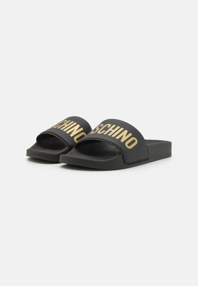 Schwarze Rutschen mit einem breiten Riemen, der mit goldenen "MOSCHINO"-Text verziert ist. Texturierter Fußbett und flache Gummisohle für Komfort.