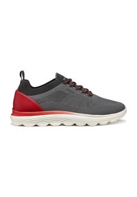 Scarpa sportiva in mesh grigia con un accento rosso sul tallone e una suola bianca texturizzata. Presenta lacci e un design con collo in maglia per un comfort aggiuntivo.