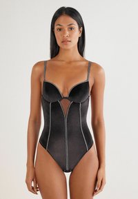 Sort bodysuit med en dyb udskæring, formede kopper, gennemsigtig panel og kontrastfølgende sølvtråd. Stropperne kan justeres.