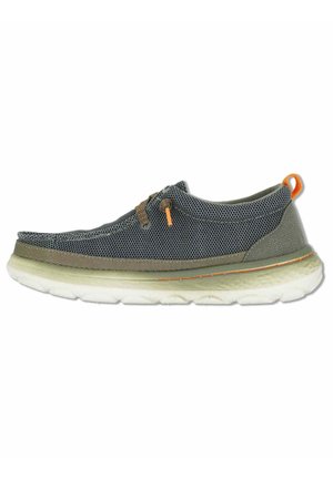 Zapatilla deportiva casual gris y oliva sin cordones con suela blanca gruesa, cordones elásticos marrones y lengüeta naranja en el talón, mostrada de perfil.