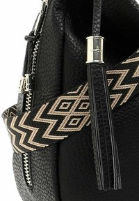 Sac en cuir noir texturé avec une sangle à motif zigzag noir et beige, et des détails de fermeture éclair et de fermoir en argent.