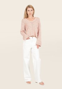 Un pull cropped en tricot rose clair avec un motif complexe et des manches cloche longues, associé à un pantalon large blanc et des sandales à lanières.