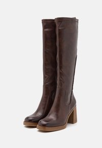 Ruske kožne čizme do kolena sa masivnom drvenom petom, glatke teksture, zaobljenim prstima i bočnom elastikom za lakše obuvanje.