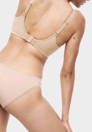Reggiseno beige con spalline regolabili e chiusura a gancio, abbinato a bikini coordinato, che mette in risalto la texture liscia e il design minimale.