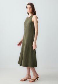 Robe sans manches vert olive en lin, présentant une coupe droite, une longueur mi-mollet et des détails de couture verticale subtils.