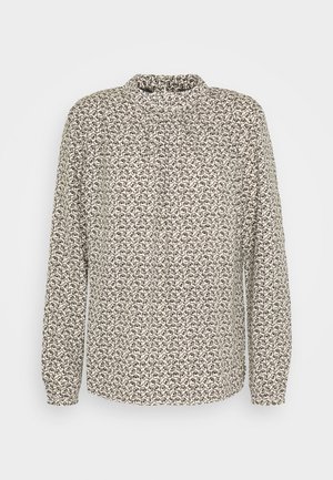 Blouse à manches longues beige, arborant un motif abstrait noir et marron répétitif, col haut et tissu doux avec une légère texture.