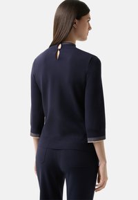 Navy Stricktop mit Dreiviertelärmeln, einem Rückenschlüssellochdetail und gestreiften Akzenten an den Bündchen und dem Saum. Glatte Textur.