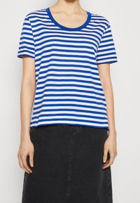 Camiseta de manga corta a rayas azul y blanca con escote redondeado, hecha de una suave mezcla de algodón, combinada con una falda de mezclilla negra.