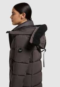 Chaqueta de plumas de color gris oscuro con un cuello de piel sintética negra texturizada, cierre de cremallera y herrajes de marca en la manga. Vista lateral.