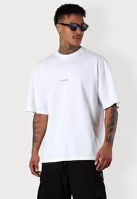 White cotton t-shirt with a relaxed fit, featuring a small "ESTEEM" logo in the center. Short sleeves and a round neckline. Hidden tag detail.