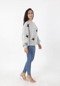 Grijze gebreide trui met zwarte stermotieven, oversized pasvorm, geribde manchetten, gecombineerd met blauwe skinny jeans en doorschijnende hak sandalen.
