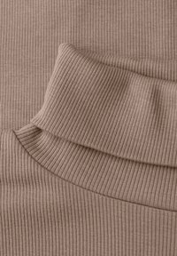 Close-up van zacht geribd stof, gevouwen om de textuur en naden in een gedempte beige kleur te accentueren.