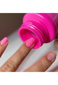 Helderroze nagellakfles met een brede, ronde opening, en een vinger die de lak aanbrengt. De nagels zijn netjes gepedicured in een bijpassende kleur.