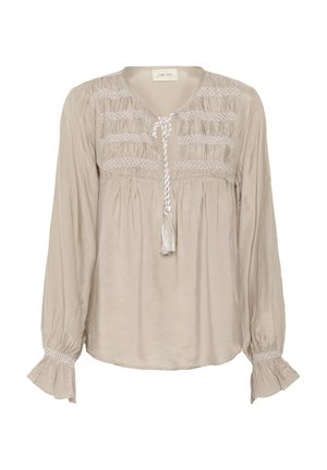 Beige blouse met lange mouwen, geplooide details bij het lijfje en een kwastje als strik. Bevat textuuraccenten langs de mouwen.