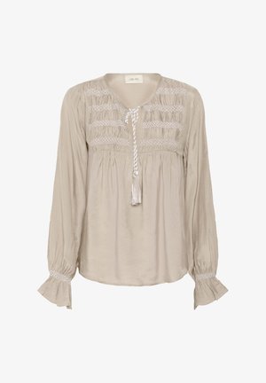 Blusa beige con maniche lunghe, dettagli arricciati sul corpino e un laccio con nappine. Presenta inserti testurizzati lungo le maniche.