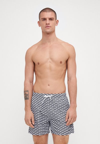 Costum de baie cu model alb-negru, cu talie elastică și șnur, fabricat dintr-un material ușor. Prezintă un design cu valuri.