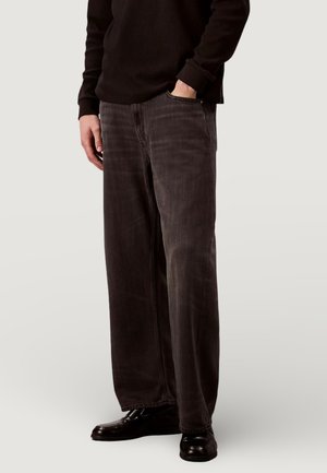 Jeans a gamba larga di colore grigio scuro in denim, con il classico design a cinque tasche e lievi effetti usurati, abbinati a scarpe nere lucide.