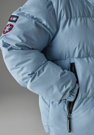 Hele sinine puffertagi, millel on tikanditooted, elastsed mansetid ja must tõmblukk. Peal on logod õlal ja varrukal.