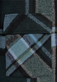 Ciemnozielona i niebieska tkanina w kratę o puszystej teksturze; posiada kwadratową kieszeń naszywaną oraz przekątne linie w jaśniejszych odcieniach.