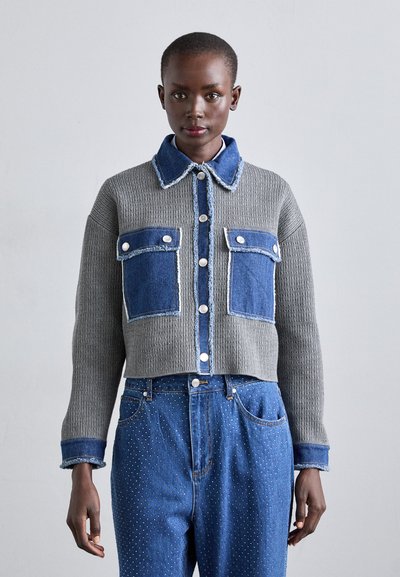 Jachetă croppată din material tricotat gri cu accente din denim albastru, inclusiv două buzunare frontale și detalii contrastante la nasturi.