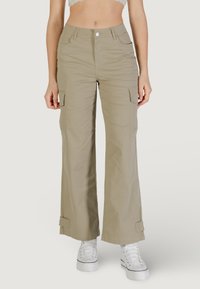 Pantalones cargo beige con corte relajado, bolsillos laterales y dobladillos ajustados, hechos de una tela ligera. Combinados con zapatillas blancas.