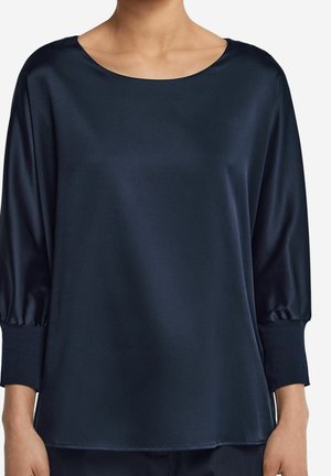 Femme portant un chemisier ample en satin bleu marine foncé avec manches trois-quarts et col rond sur un fond clair.