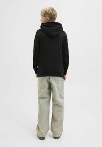 Felpa nera con cappuccio e tasca a marsupio, abbinata a pantaloni larghi di un verde chiaro. L'outfit ha un design semplice e rilassato.