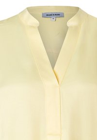 Gele blouse met een V-hals, gemaakt van gladde stof. Heeft een kraag, subtiele stikseldetails en het merklabel zichtbaar aan de binnenkant.
