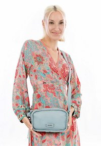 Borsa a tracolla in pelle azzurro chiaro con dettagli intrecciati, forma rettangolare e tracolla regolabile, tenuta da una persona che indossa un vestito floreale.