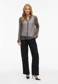 Doorzichtig grijs button-up blouse met lange mouwen, gecombineerd met gestructureerde zwarte wijde broek en spitse zwarte hakken.