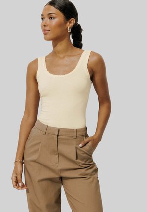 Un débardeur couleur crème avec un col festonné associé à un pantalon plissé beige clair, présenté sur un fond neutre.