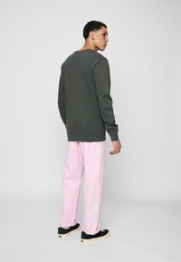 Hanorac gri cu guler rotund, asortat cu pantaloni roz deschis. Încălțămintea are partea superioară neagră și talpa bej. Design simplu, fără modele.