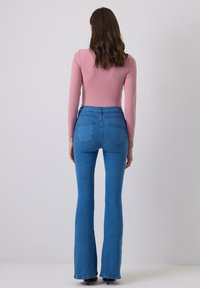 Jeans biru lebar dengan pinggang tinggi, terbuat dari denim, memiliki saku belakang dan permukaan yang halus. Dipadukan dengan atasan lengan panjang berwarna merah muda.