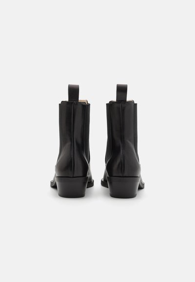 Botas de tobillo de cuero negro con una textura suave, paneles laterales elásticos y una etiqueta en la parte posterior. Tacón apilado de aproximadamente 3 cm de altura.