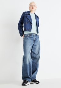 Jeansjakke med en cropped design, store revers og messingknapper, kombinert med en stripete lyseblå skjorte og løse blå jeans. Svarte sneakers.