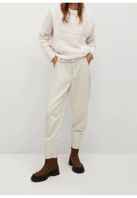 Pull en maille rose clair avec des motifs texturés, pantalon ample couleur crème, et bottines marron foncé avec une épaisse semelle noire.