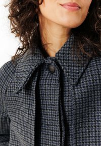 Manteau en laine à motif pied de poule en bleu marine et gris, présentant un large col, une fermeture à boutons et un tissu texturé.