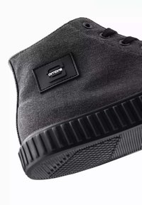 Zapatilla alta de lona negra con tejido texturizado, puntera redonda y suela de goma. Presenta un parche con el logo negro y diseño de cordones.