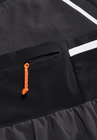 Svart sportjacka med en dragkedjeficka som har en orange draggrepp. Den har vita detaljer och en texturerad tygfinish.