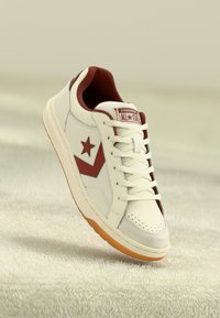 White leather sneaker with a maroon star and accent. Features a lace-up front, a textured sole, and a logo patch on the tongue.