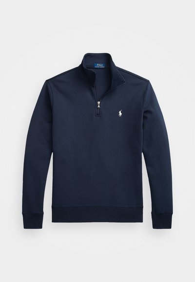 Marineblå kvart-zip genser med en glatt tekstur, ribbet mansjetter og en liten hvit logo på venstre bryst. Merkesignatur inne.