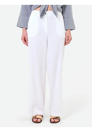 Femme portant un pantalon blanc taille haute à jambes larges, associé à des sandales marron et une chemise rayée nouée laissant voir le ventre.