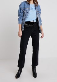 Džínová bunda, světle modré tričko s logem "GUESS", černé džíny s vysokým pasem a černé kotníkové boty. Černá ledvinka s detaily zapínání.