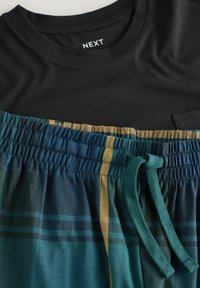 Musta pyöreäkauluksinen paita yhdistetty sinivihreisiin ruudullisiin housuihin, joissa on joustava vyötärö ja petroolinvihreä nyörö.