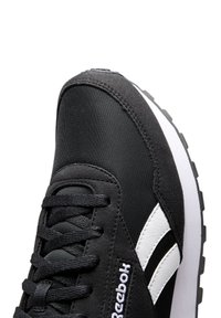 Zapatilla deportiva negra con una parte superior texturizada, acentos blancos y cordones. Presenta una suela de goma gruesa y un logo en el lateral.
