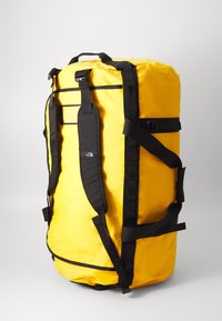 Bolsa de lona amarilla con correas negras, con forma cilíndrica, material sintético duradero, asas laterales y correas de hombro ajustables.
