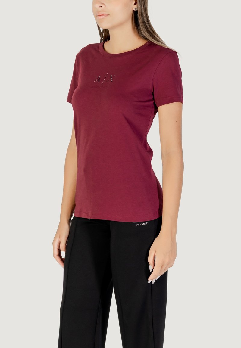 T-shirt corto color bordeaux in tessuto morbido con scollatura rotonda, con dettaglio del logo glitterato sul davanti, abbinato a pantaloni a gamba larga neri.